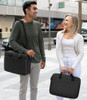 A man with a backpack laughing at a woman who is also smiling while holding a laptop case.